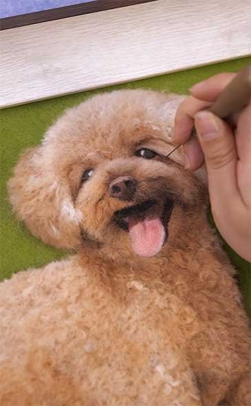 Close-up of a professional artist meticulously needle felting a custom pet portrait, showing the intricate process of shaping natural wool fibers with a specialized felting needle.