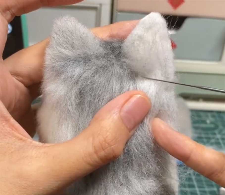 Artisan hands creating custom stuffed animals using needle felting technique, showing the intricate process of shaping wool fibers.