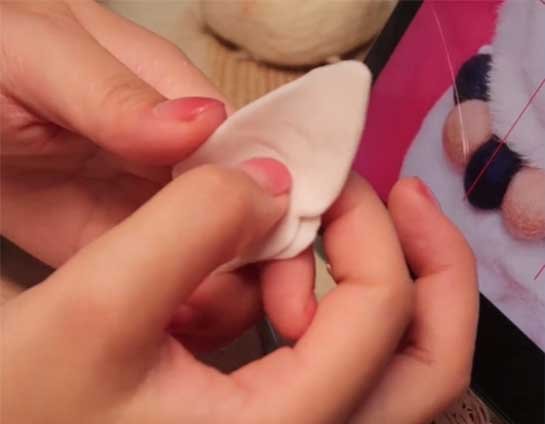 Shaping a thin resin clay triangle with a small side notch to simulate the anatomical ear profile for a custom needle felted pet sculpture.
