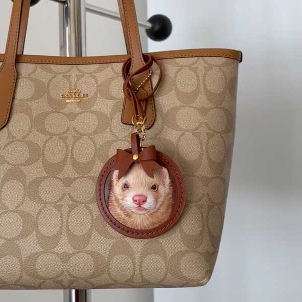A detailed Ferret / Mink leather carving tag made from vegetable-tanned hide, hanging on a luxury handbag as a sustainable fashion charm for pet lovers who prioritize eco-friendly leather custom pet gifts.