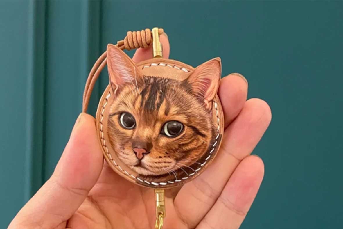 A hand holding a custom 3D hand-carved vegetable-tanned leather cat portrait, showcasing artisanal leather craft and natural patina texture.