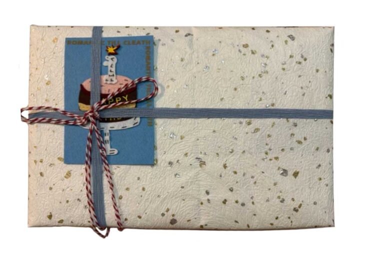 Elegantly wrapped custom pet memorial gift featuring textured artisan paper, a blue ribbon, and a "Happy" cake illustration card.