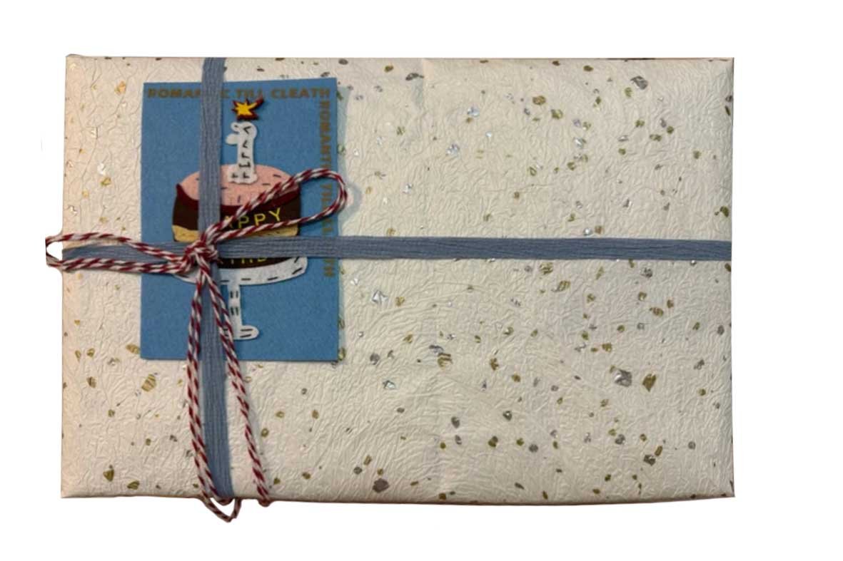 Elegantly wrapped custom pet memorial gift featuring textured artisan paper, a blue ribbon, and a "Happy" cake illustration card.