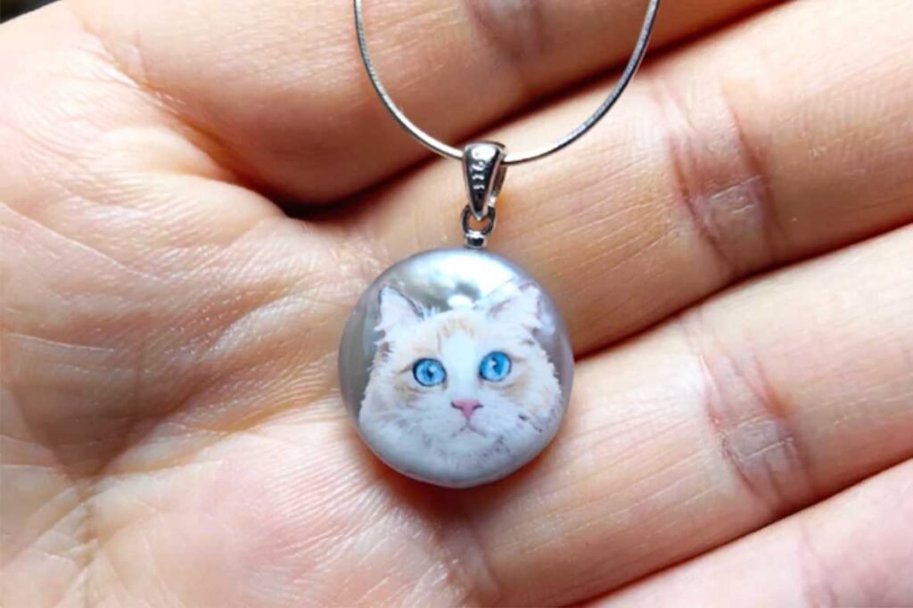 Detailed hand-painted blue-eyed cat portrait on a grey pearl necklace, perfect as a cat mom gift or pet memorial.