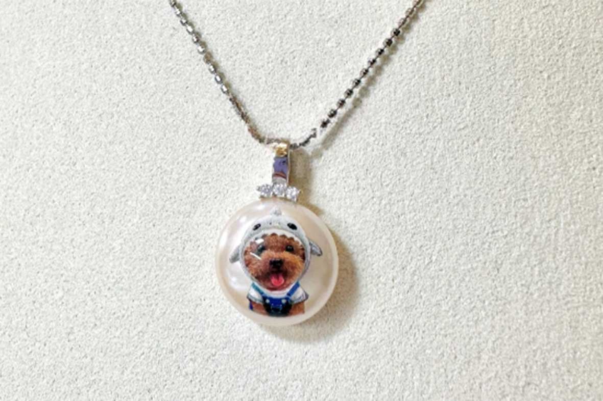Custom handmade pet necklace featuring a miniature hand-painted poodle portrait on a pearl-like pendant with a silver chain.